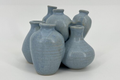 Cluster of light blue matte ceramic vases with rounded bodies, piled together on a pale surface.