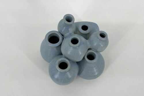 Pile of small blue-gray ceramic vases with open circular mouths.