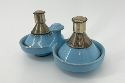 Two light-blue ceramic bases with metal threaded spouts and knurled collars, resting on a white surface in a close-up shot.