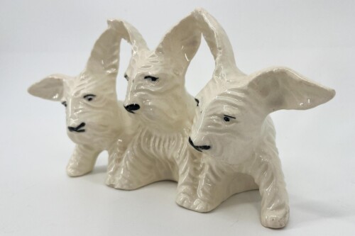 Three glossy white ceramic dog figurines standing together, facing different directions.