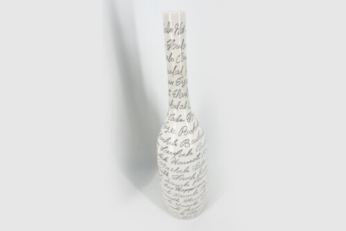 Tall white ceramic vase with black cursive handwriting all over, standing upright against a light background.