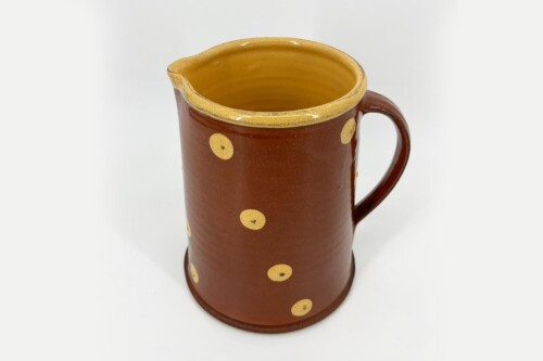 Brown ceramic pitcher with yellow polka dots and a yellow rim, on a white background/surface. (informative)