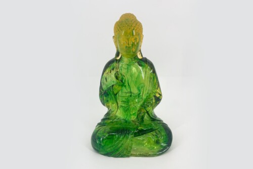 Green glass Buddha statue in meditation pose with a yellow-tinged head, translucent and serene.