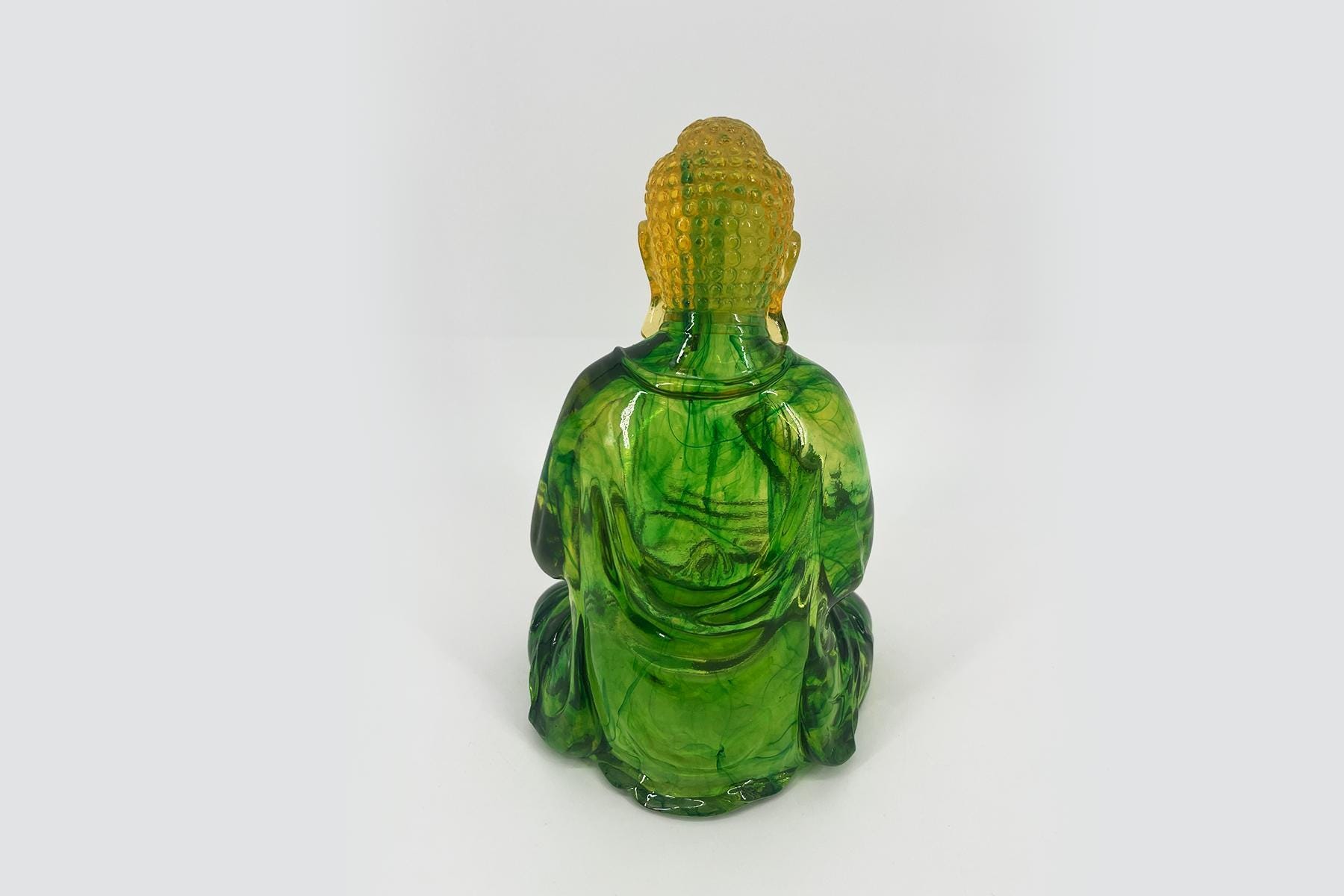 Back view of a seated Buddha statue made of translucent green glass.