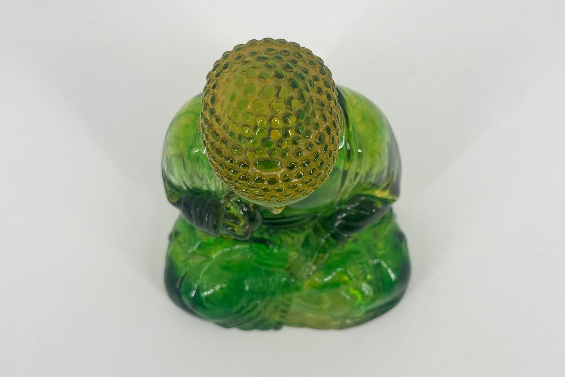 Top-down view of a green glass frog sculpture with a bumpy yellow-green head and translucent body.
