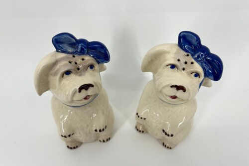 Two cream-colored ceramic dog figurines with blue hats facing slightly inward.