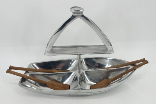 Three-tier silver serving stand with cinnamon sticks laid across the trays behind the pyramid-top handle.