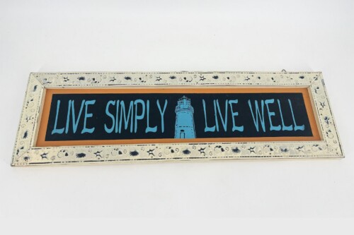 Decorative framed sign reading 'Live Simply Live Well' with a blue lighthouse between words.