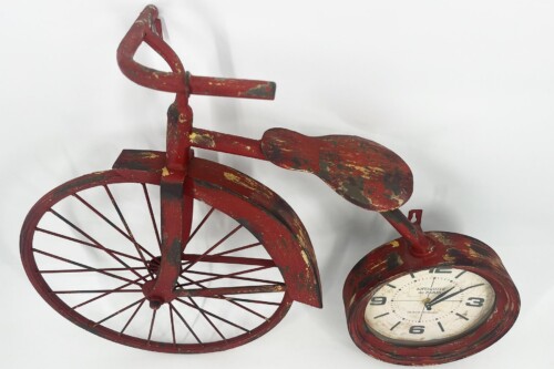 Decorative red vintage tricycle sculpture with peeling paint and a round clock integrated in place of the front wheel