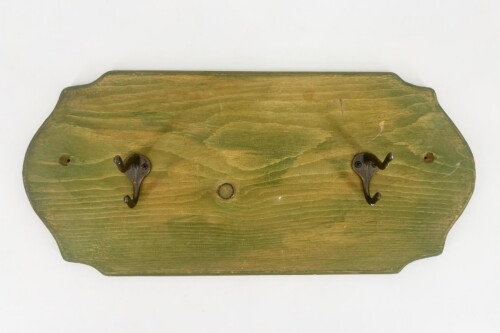 Green wooden wall plaque with scalloped edges and two black metal hooks for hanging items