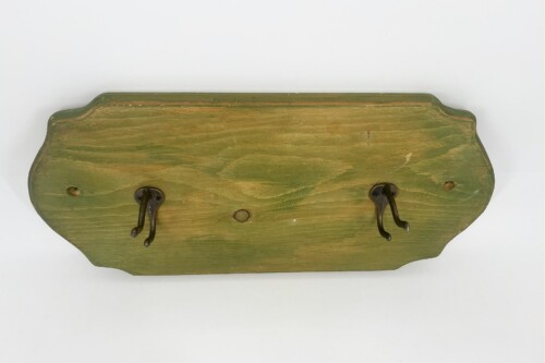 Weathered green wooden plaque with two dark metal hooks for hanging items, mounted to a wall.