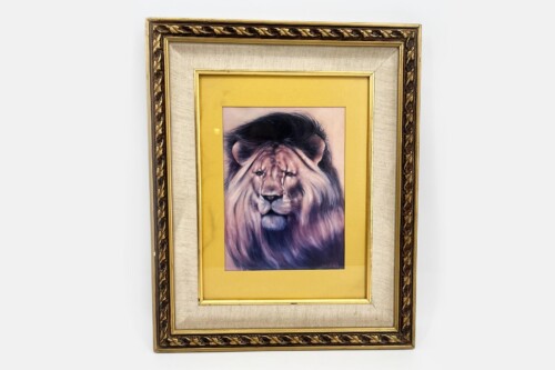 Portrait of a lion in a gold frame with a yellow mat, hanging on a light background.