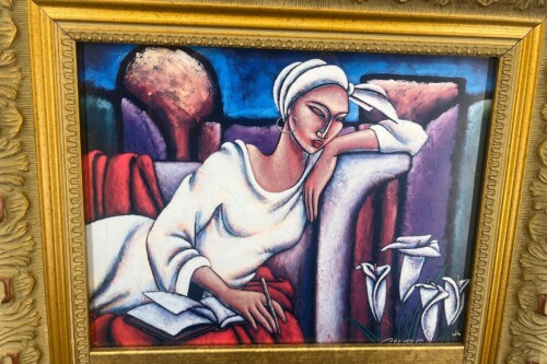 Stylized painting of a woman in a white dress and head wrap, leaning on a couch and writing on paper, with a blue background behind her.