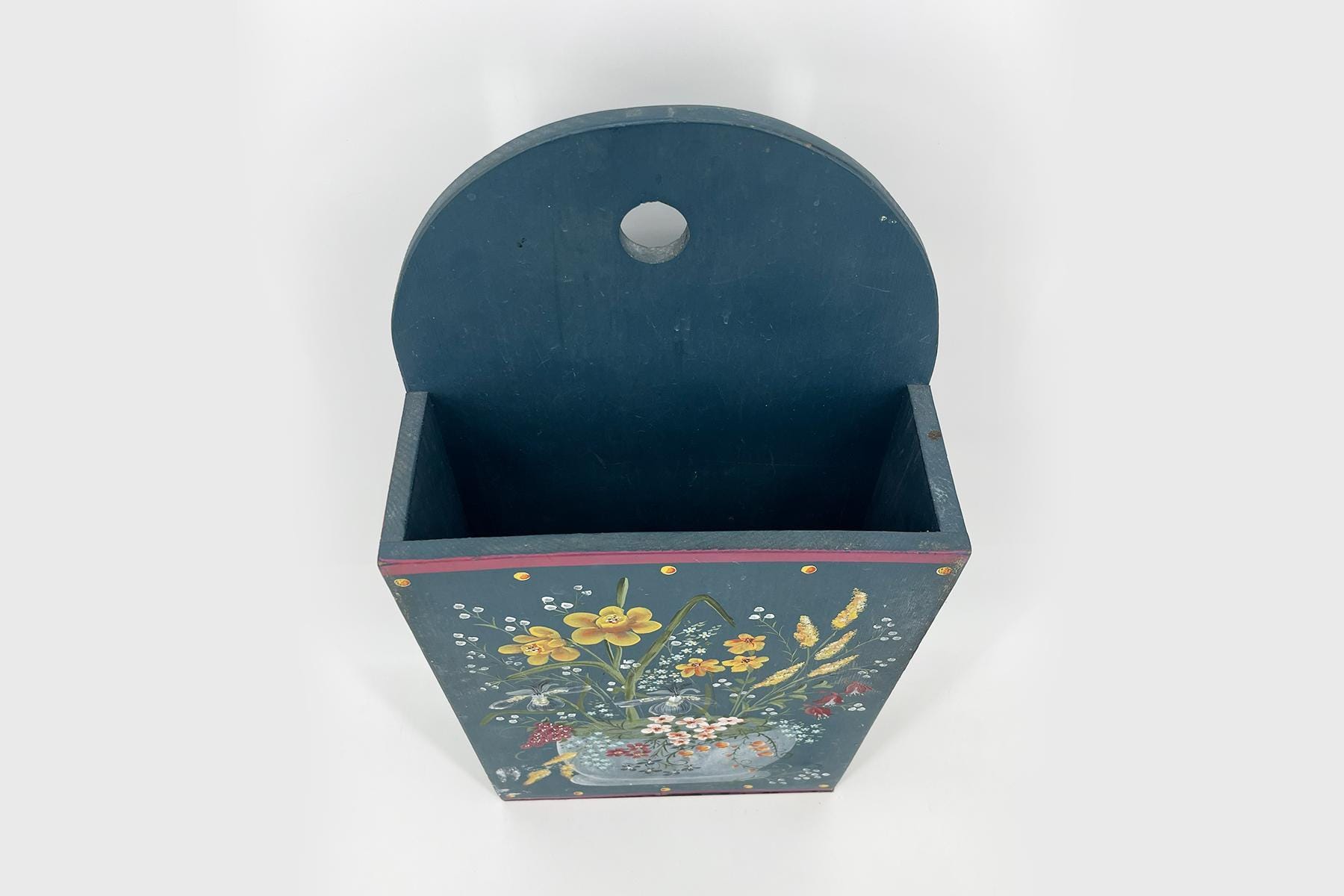 Blue-painted decorative wooden box with an open top, featuring a floral bouquet on the front and a circular hole in the back panel.