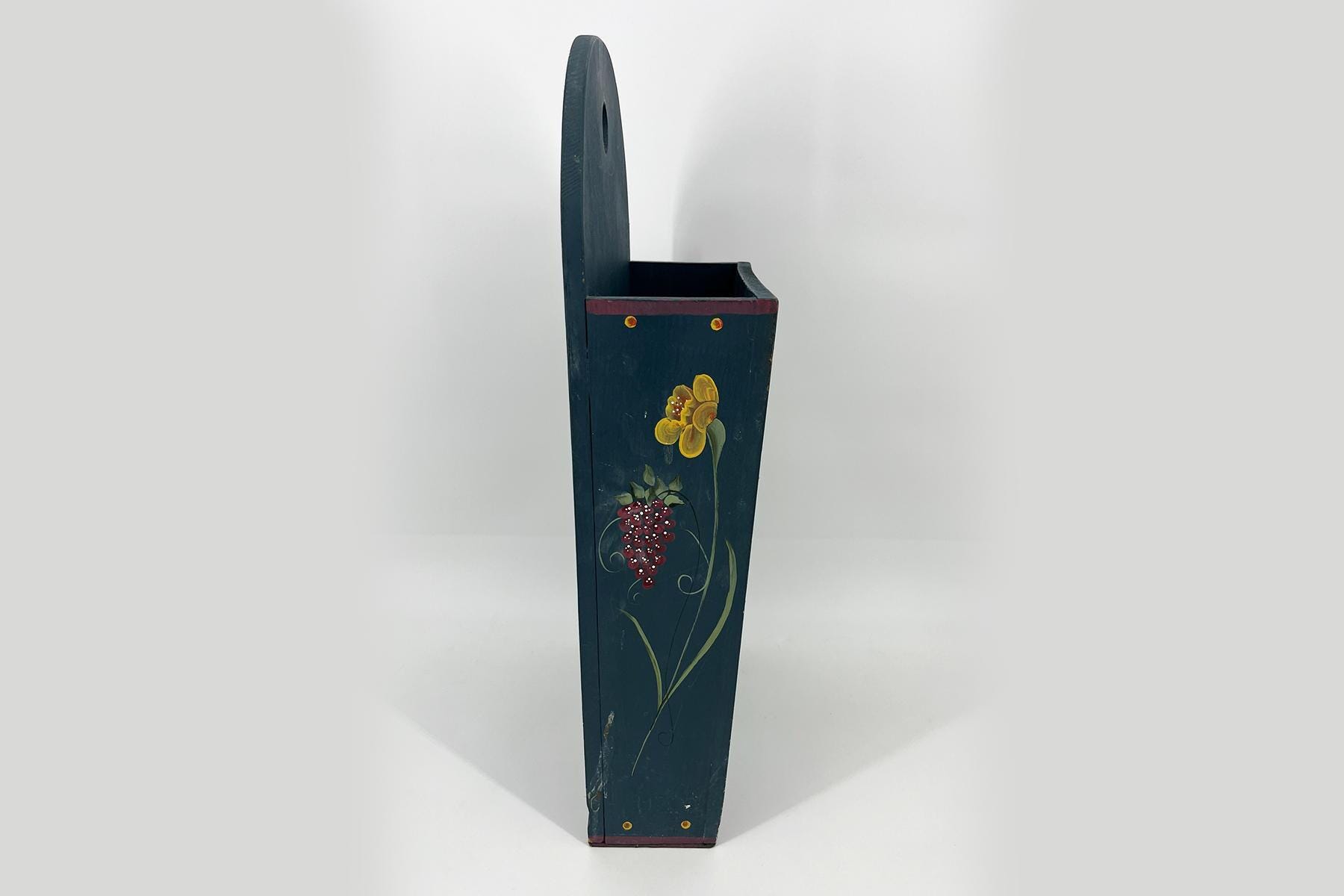 Tall dark-blue wooden decorative piece with a curved back and an open top, hand-painted with yellow flowers and red berries.