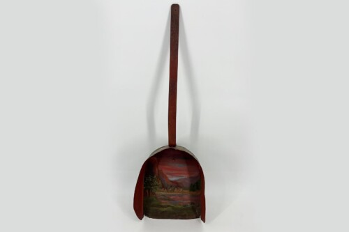 Rust-red abstract sculpture with a long vertical rod extending upward from a round, painted landscape relief at the bottom.