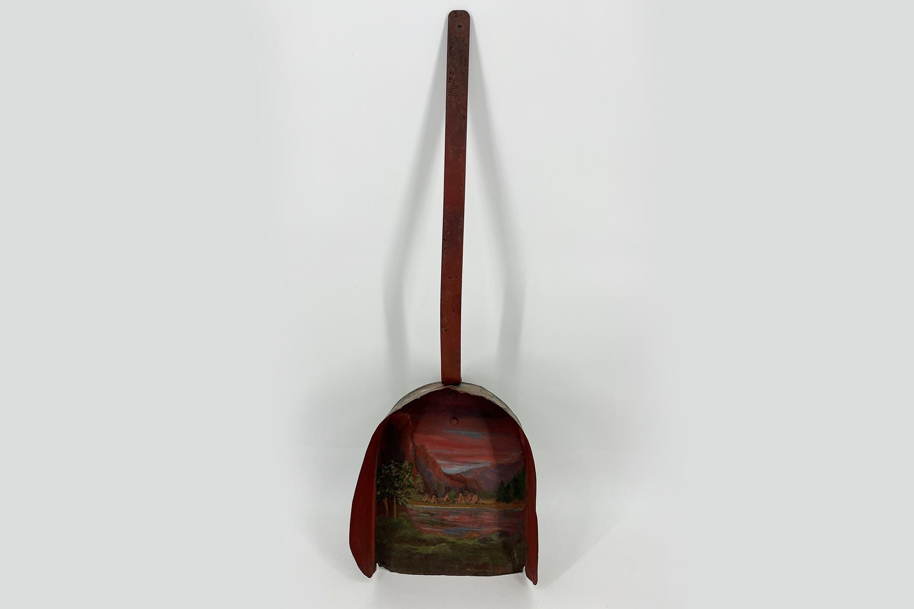 Rust-red abstract sculpture with a long vertical rod extending upward from a round, painted landscape relief at the bottom.