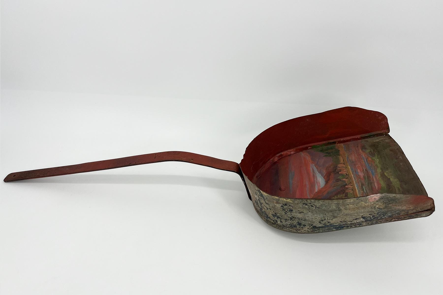 Antique red metal coal iron with a long curved handle, showing rust and wear on a white surface
