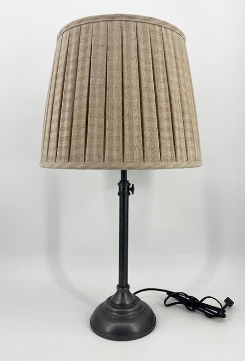 Table lamp with a black metal stand and a beige pleated shade on a white background, cord visible.