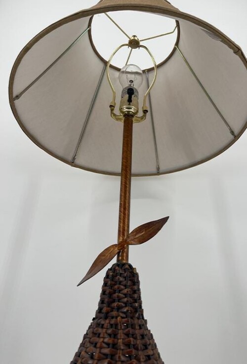 Vintage-style floor lamp with a wide beige fabric shade, wooden pole, and a woven wicker cone base with a leaf-shaped accent wrapping around the stem.