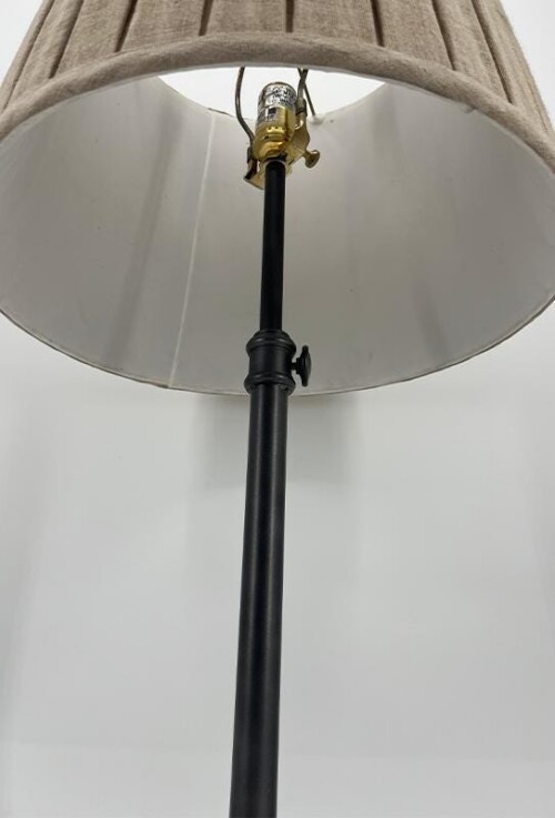 From below, a tall black floor lamp with a beige fabric shade and visible lamp socket at the top of the pole.