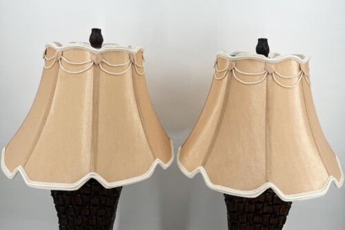 Pair of beige fabric lamp shades with white rope trim and piping atop dark wicker bases.