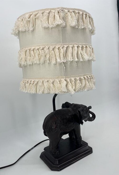 Table lamp with a carved black elephant base and a cream fringe lampshade.