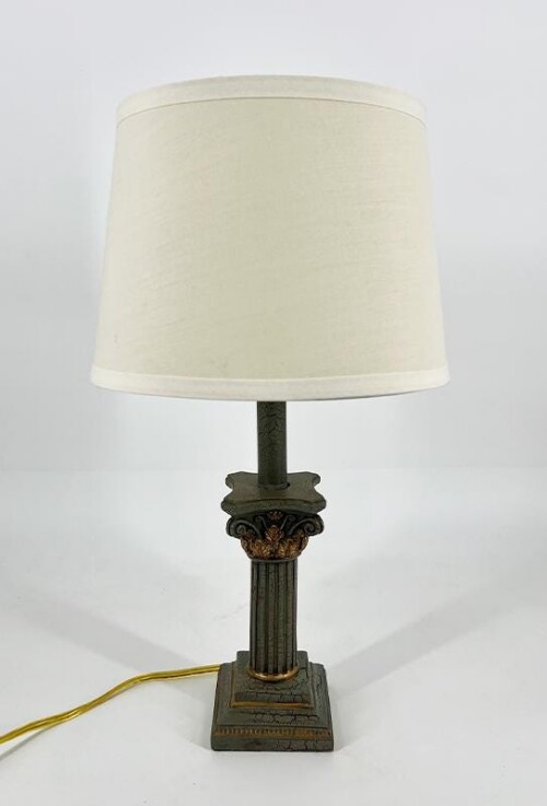 Decorative metal table lamp with a cream fabric shade and ornate base on a square pedestal.