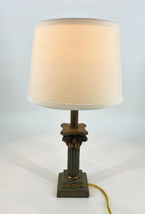 Ornate vintage table lamp with a cream fabric shade and decorative column base on a square pedestal, cord visible.