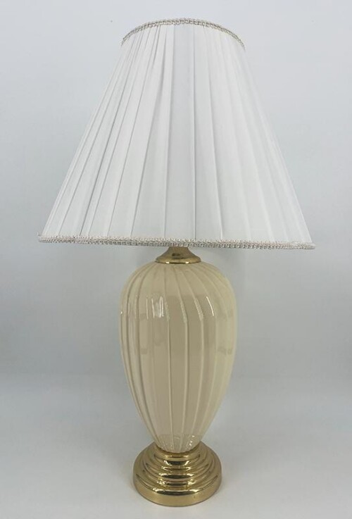 Cream ribbed ceramic table lamp with gold base and white pleated shade.