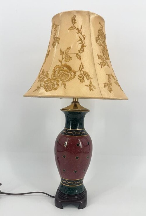 Table lamp with a burgundy ceramic body, black neck, gold trim, and a beige floral lampshade on a dark wooden base.