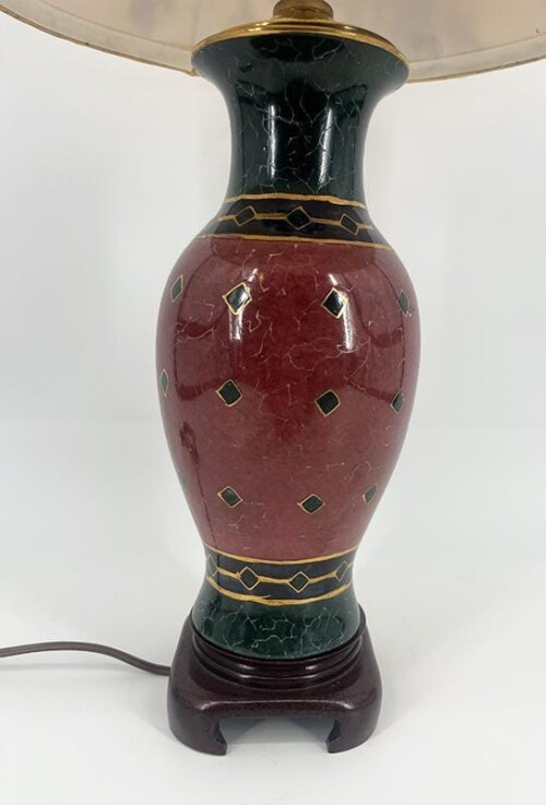 Tall ceramic table lamp base with a maroon central vase shape, green/black neck and foot, and gold geometric bands and diamonds on a wooden stand, cord visible in the background.