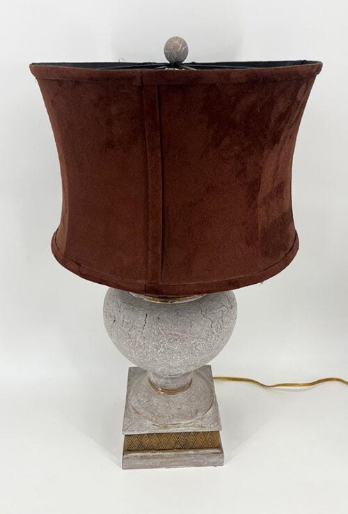 Decorative table lamp with a brown fabric drum shade atop a white marble pedestal base and an electric cord nearby.