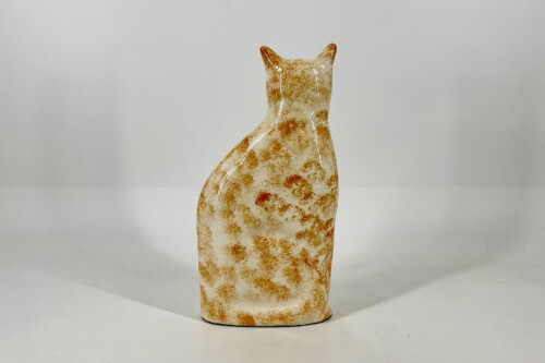 Back view of a glazed ceramic cat figurine with orange speckled pattern, sitting upright on a white surface.
