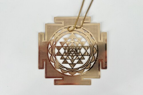 Gold pendant necklace with a circular Sri Yantra-inspired design of interlocking triangles and geometric patterns on a textured square backing.