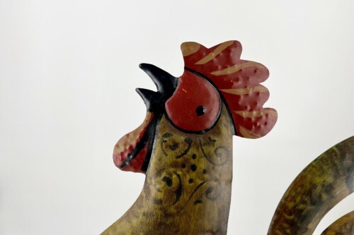 Close-up of a weathered metal rooster head with red comb and black beak, part of a decorative garden sculpture