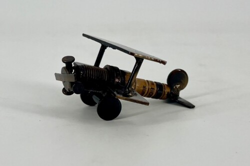Small metal toy airplane with a spring-powered engine and two wings on a white surface.