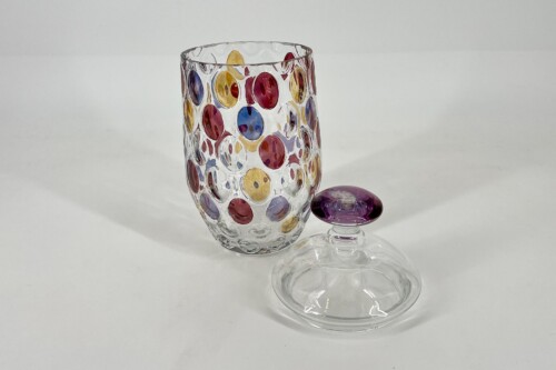 Clear glass tumbler decorated with multicolored circular dots, with a separate glass lid featuring a purple knob nearby.