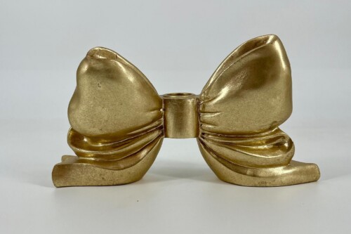Gold metallic bow figurine with curled ribbon tails on a white surface.