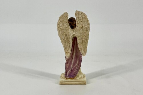 Back view of a statue: an angel with outstretched wings, standing on a small pedestal against a light background.