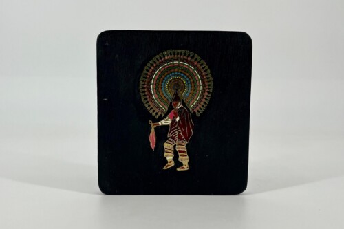 Black plaque with a colorful circular halo design behind a stylized, robed figure holding a staff