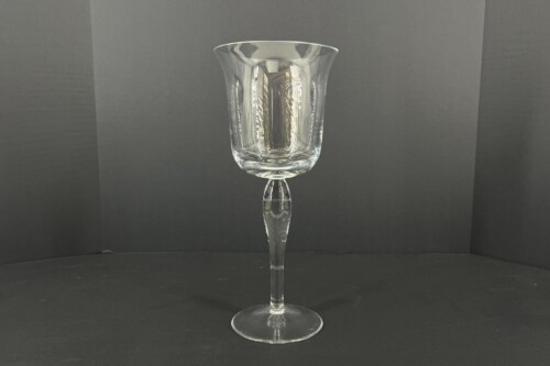 Clear stemmed wine glass centered on a dark surface with a neutral gray backdrop.