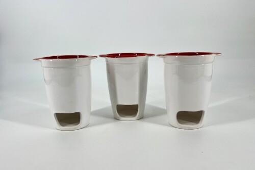 Three white ceramic cups with red-rimmed rims lined up on a white surface.