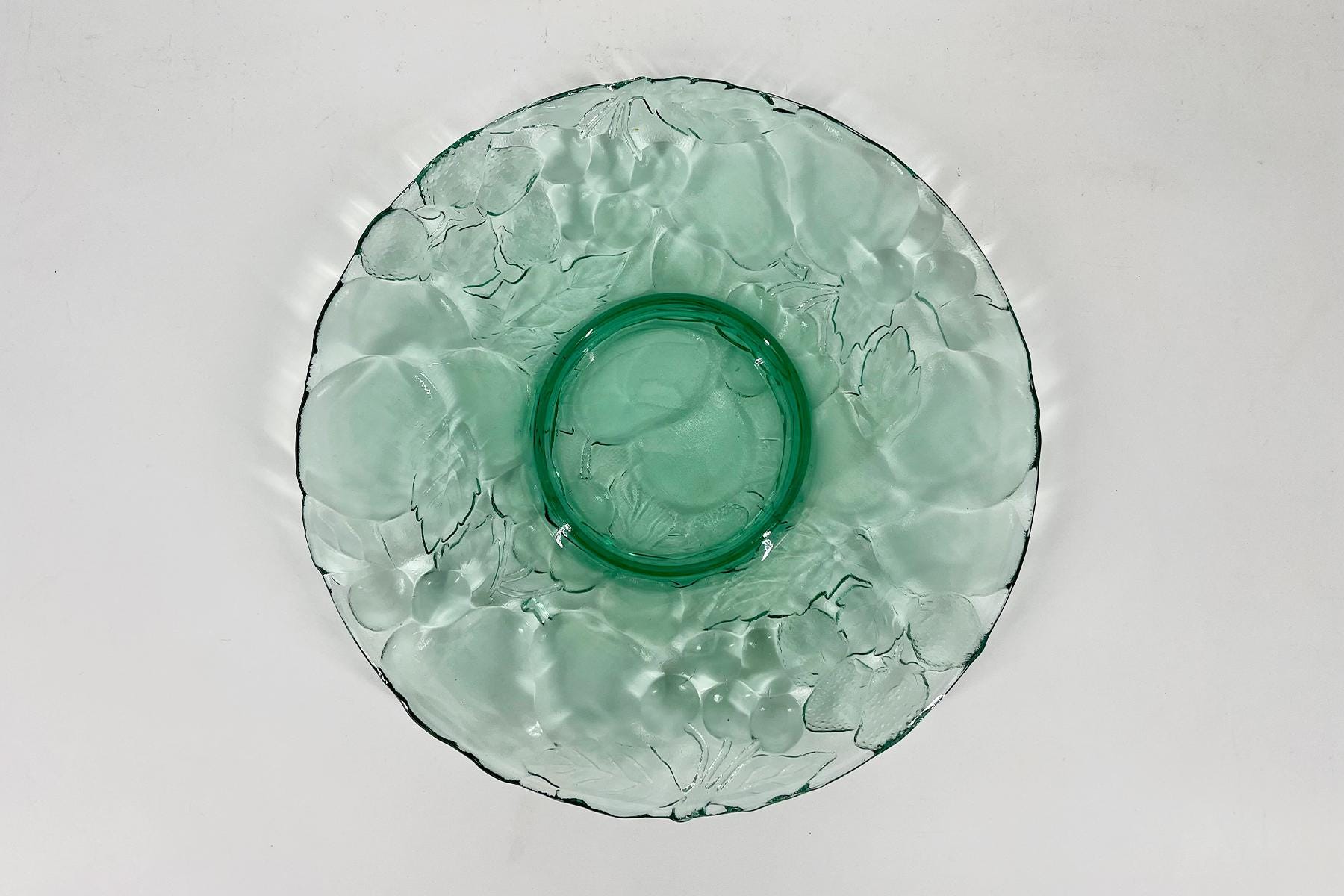 Top-down view of a pale green glass plate with a circular center and embossed floral pattern.