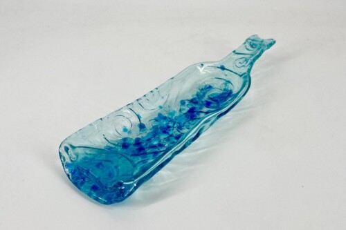 Diagonal blue glass bottle filled with blue beads and liquid on a pale surface, viewed from above.