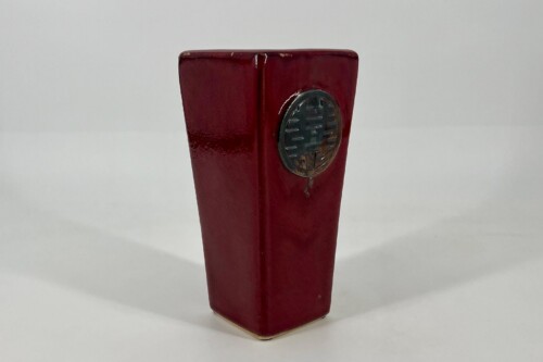 Red lacquered square post with a round silver emblem on its side (close-up).