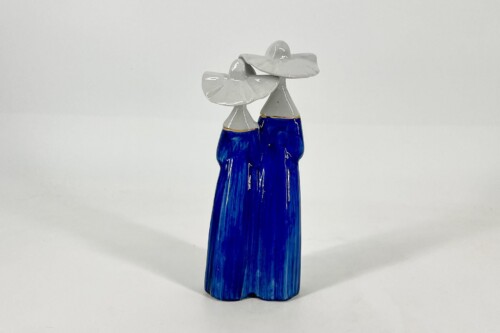 Ceramic sculpture of two abstract figures in blue robes with white heads, leaning toward each other as if embracing.