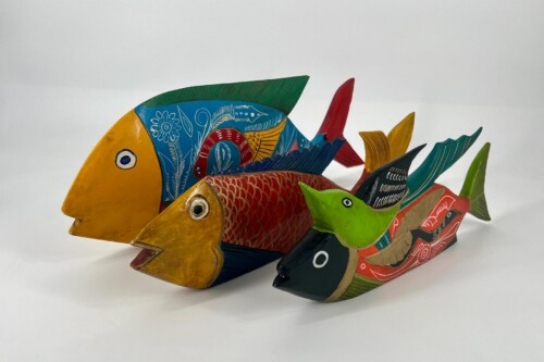 Colorful carved wooden fish sculptures stacked together, painted in yellow, blue, red, green with decorative patterns.