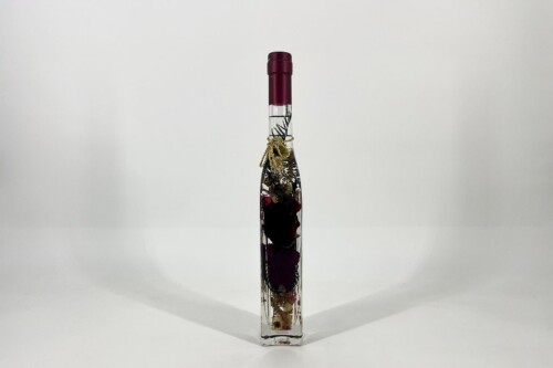 Clear glass bottle with dried flowers inside, purple cap, decorative twine at the neck, centered on a white background.