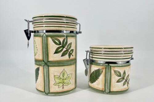 Two ceramic canisters with green leaf patterns and metal latch lids, set against a light background.